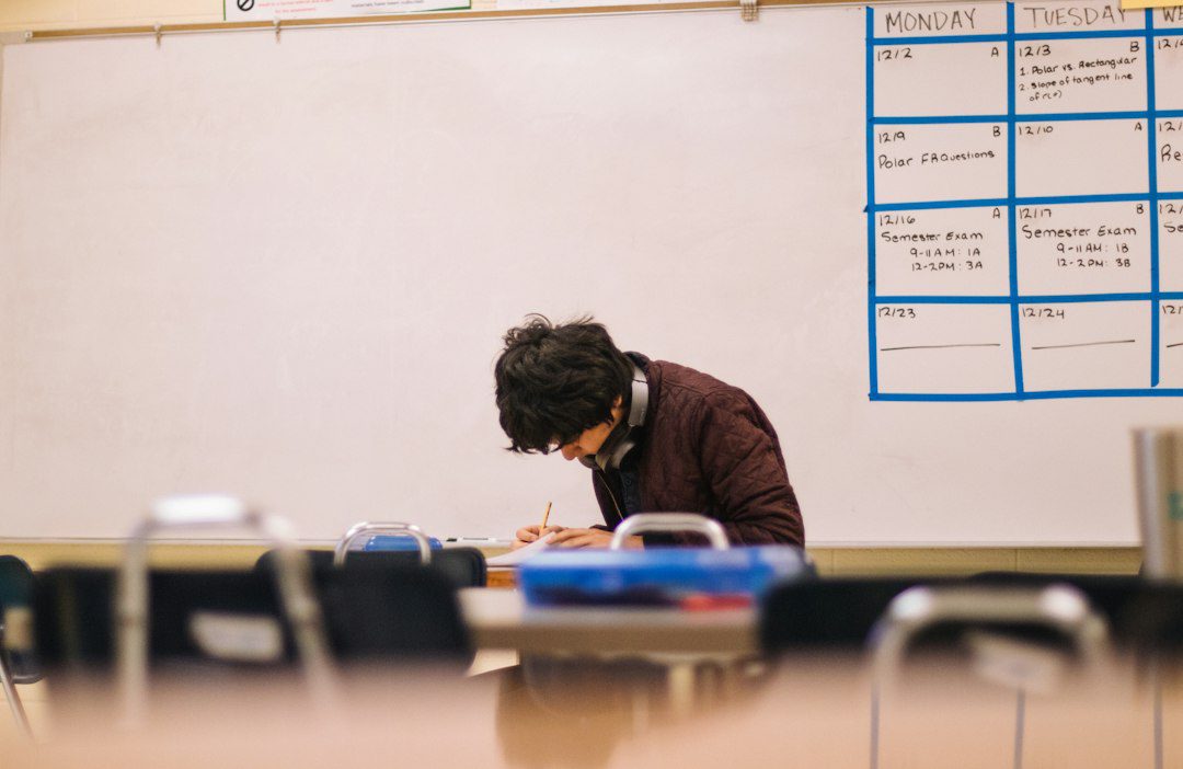 Student writing notes at a desk while calculating grades